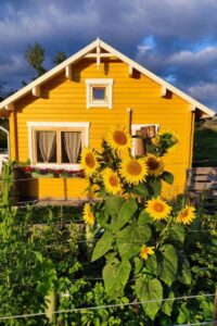 Gelbes Gartenhaus mit weißen Verzierungen und Sonnenblumen im Vordergrund