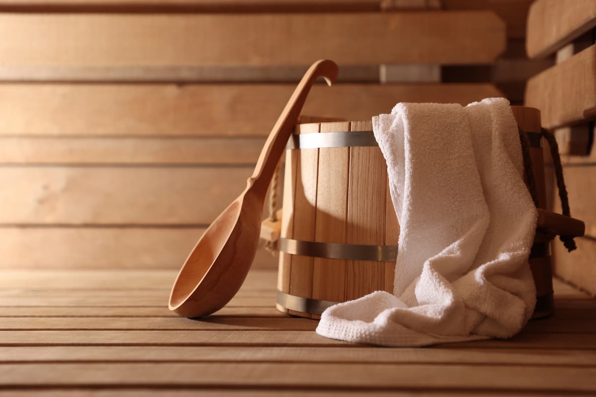 Eimer, Schöpfkelle und Handtuch auf einer Holzbank in der Sauna