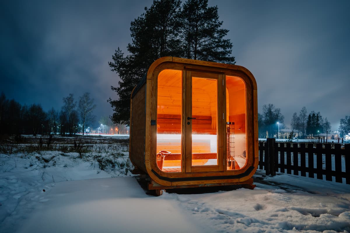 Holzsauna in einer verschneiten Landschaft bei Nacht.
