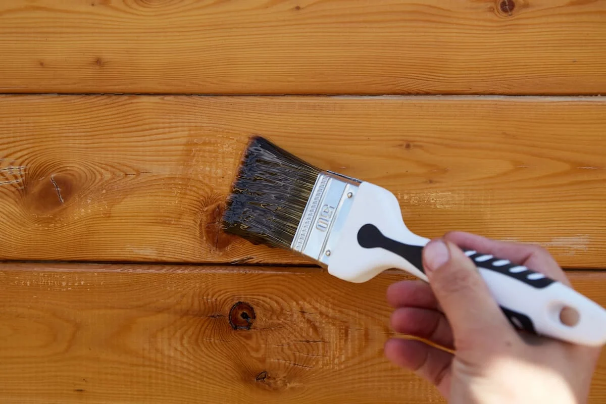 Hand mit Pinsel streicht Holzbretter bei einem Renovierungsprojekt